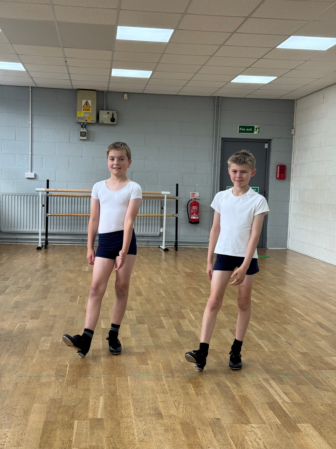 Two boys in white T-shirts and tap shoes standing ready in the studio