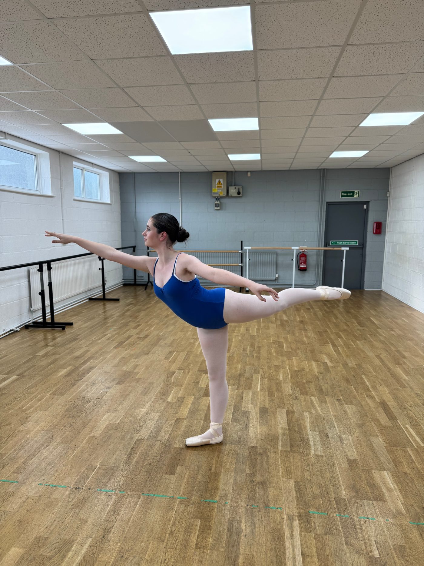 A senior student in a blue leotard holding an arabesque in the Edenfield studio